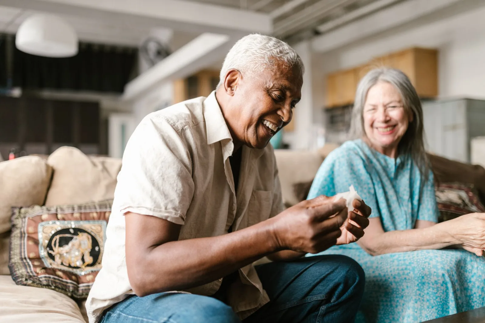 An older couple laugh together on the sofa at home.